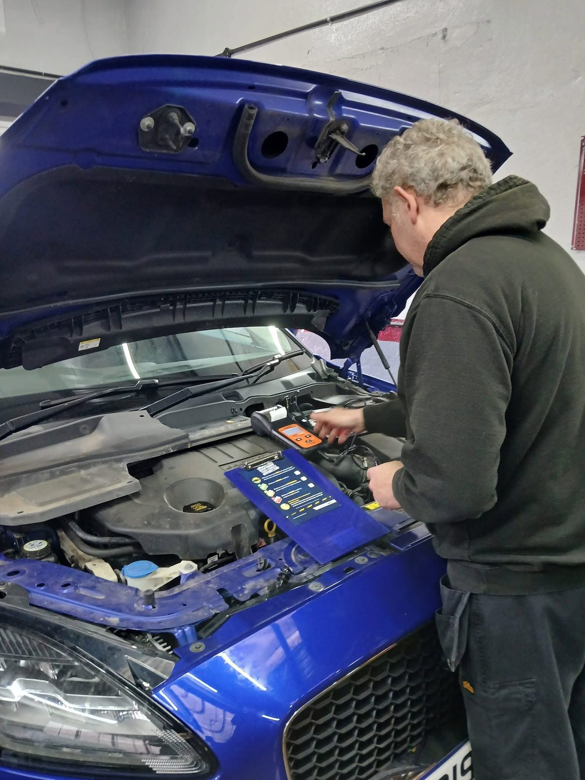 A mechanic working under the bonnet of a blue Ford in the workshop