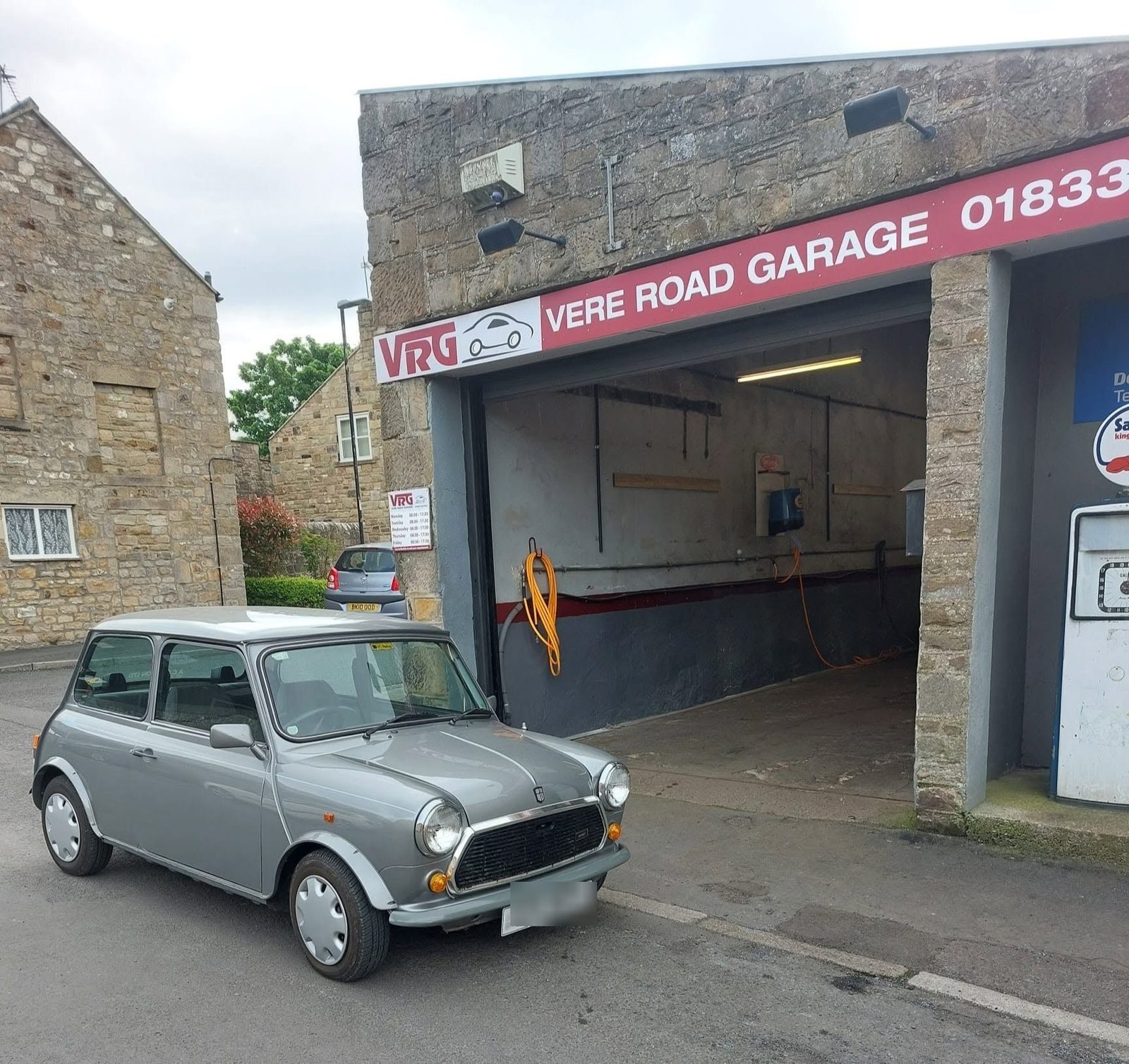 A classic Mini parked outside the open bay at Vere Road Garage, under the red VRG sign