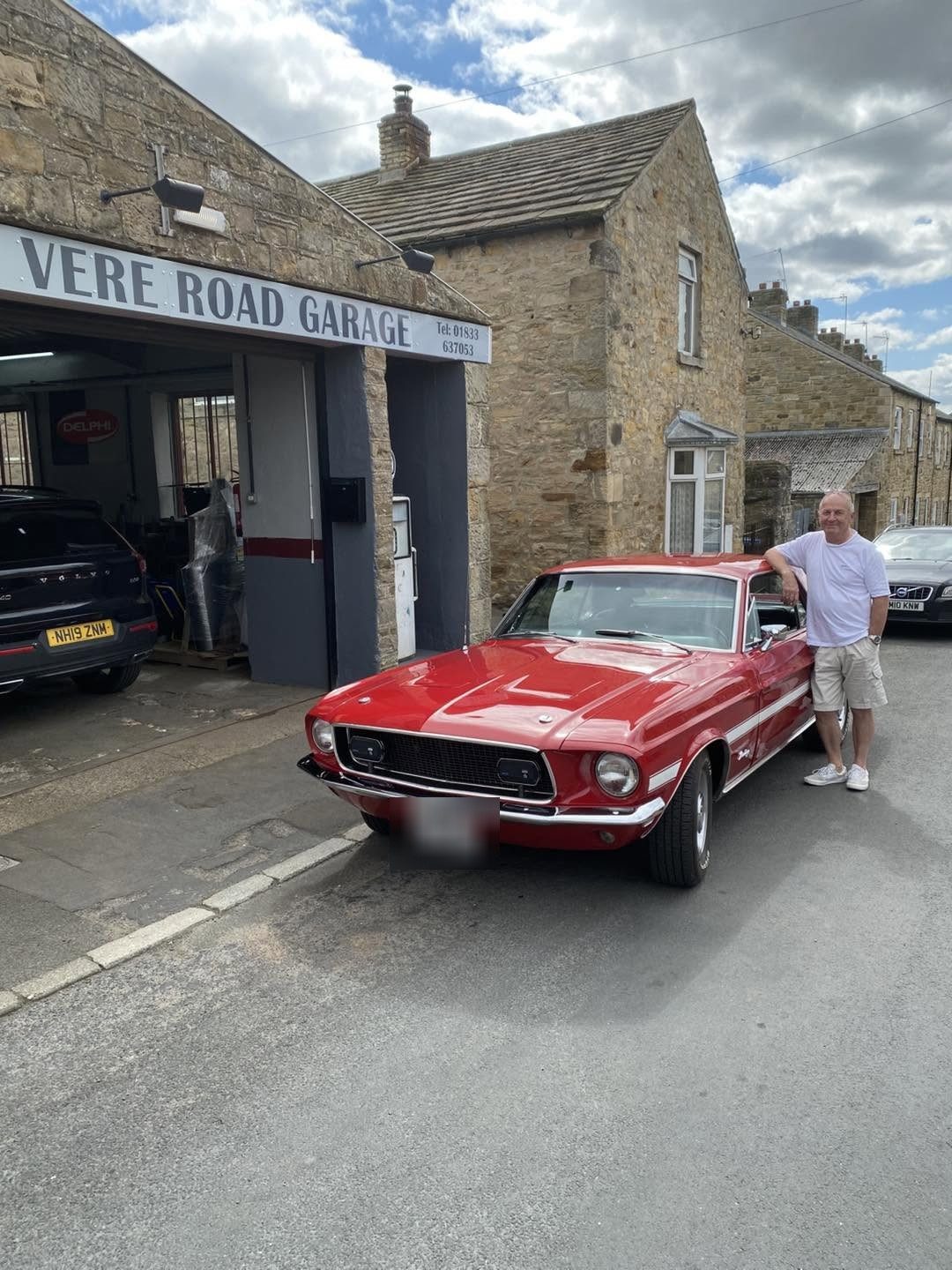 The red Mustang outside the garage with a man standing beside it