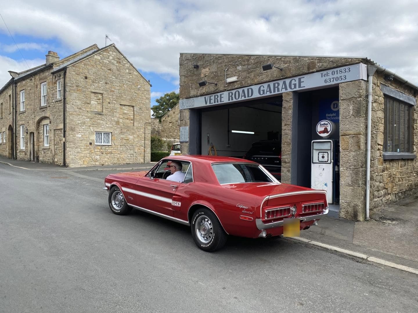 A red classic Ford Mustang on Vere Road outside the open workshop