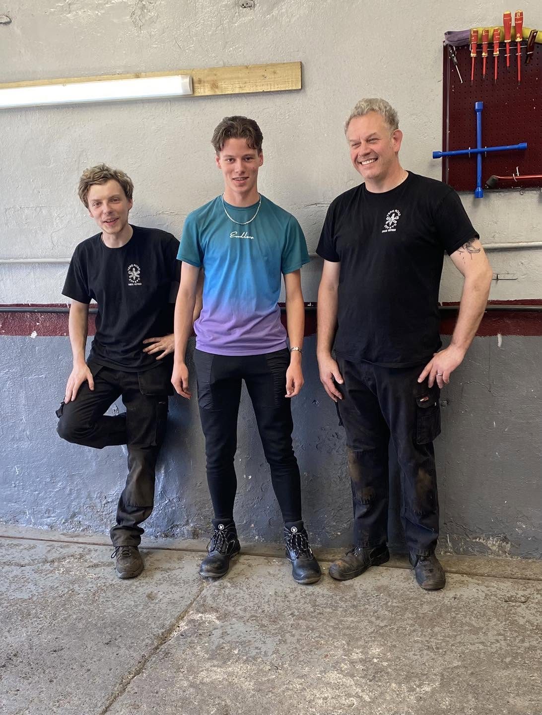 Three people standing against the workshop wall